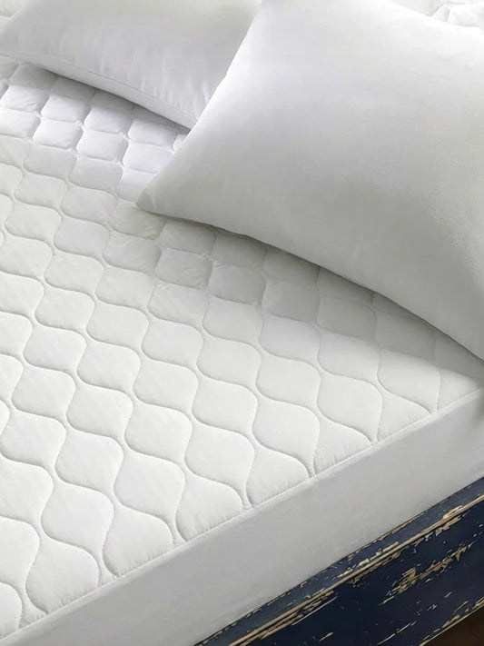 Valiant Products white quilted mattress pad with ogee pattern on a bed with pillows