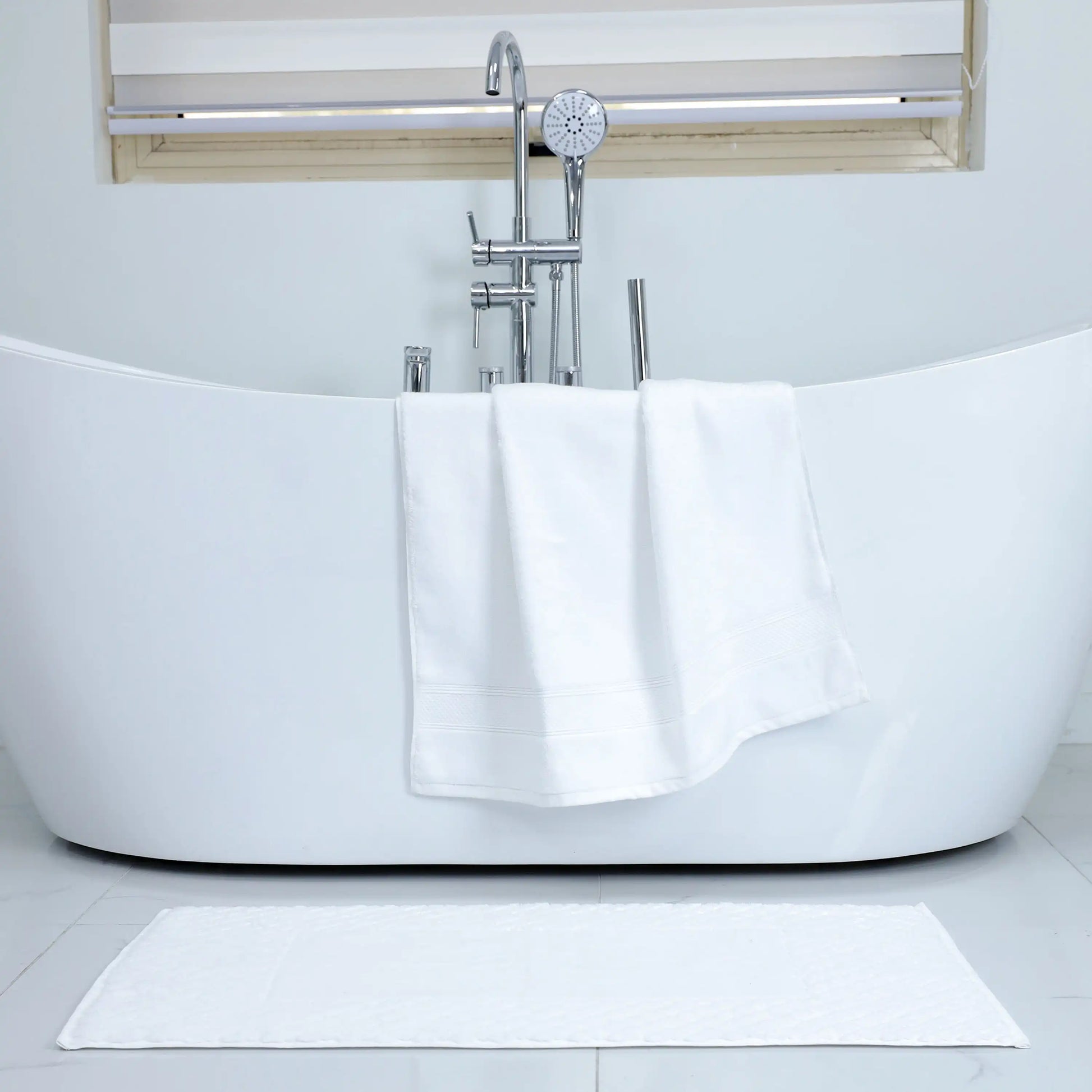 Valiant Products Atelier Zen white cotton bath towel with dobby border draped over a modern freestanding bathtub