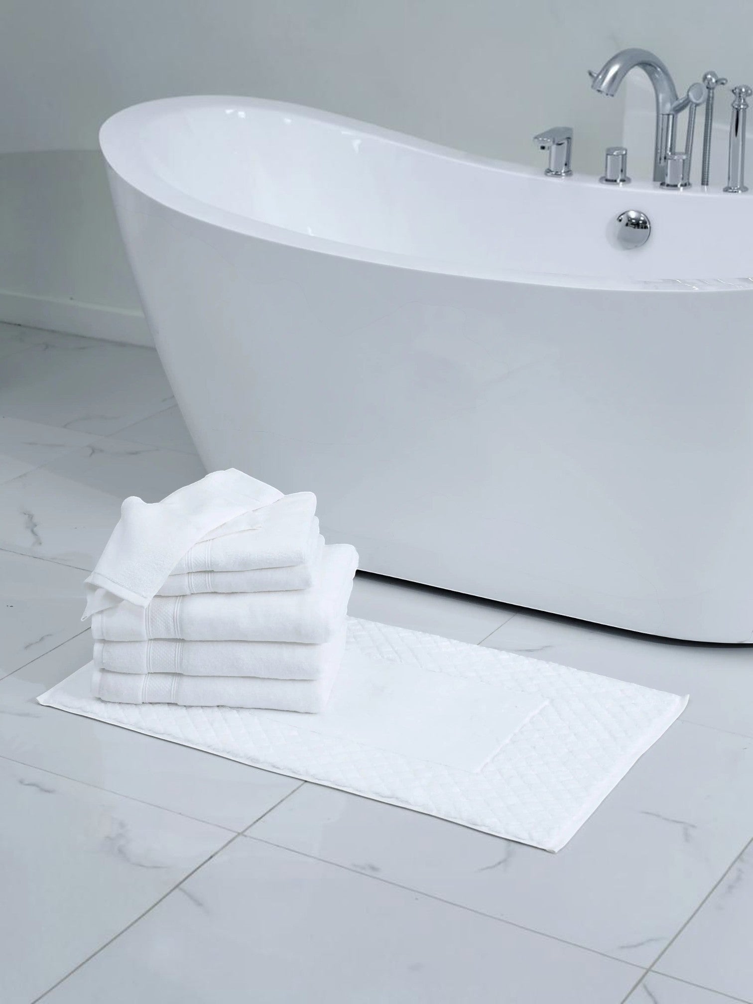 Valiant Products Atelier Zen white cotton bath towels with dobby border and diamond-frame bath mat in a bathroom.
