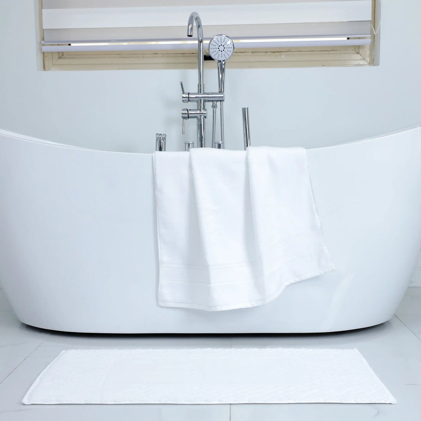 Valiant Products Atelier Zen white cotton bath mat with diamond frame design draped over a modern freestanding tub