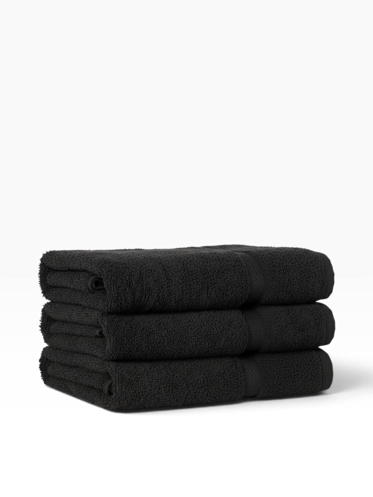 A stack of three black Valiant Products Colors dobby border bath towels made from soft ring-spun cotton.
