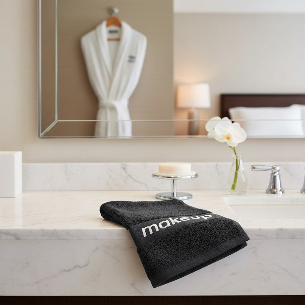 Valiant Products black cotton washcloth with a grey jacquard makeup border on a hotel bathroom vanity