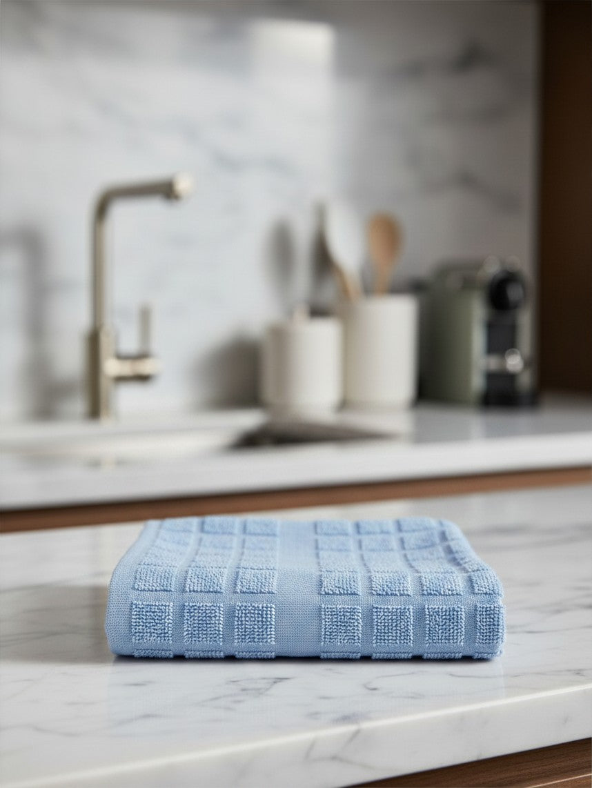 Valiant Products blue kitchen towel with a textured square pattern folded on a marble countertop in a modern kitchen