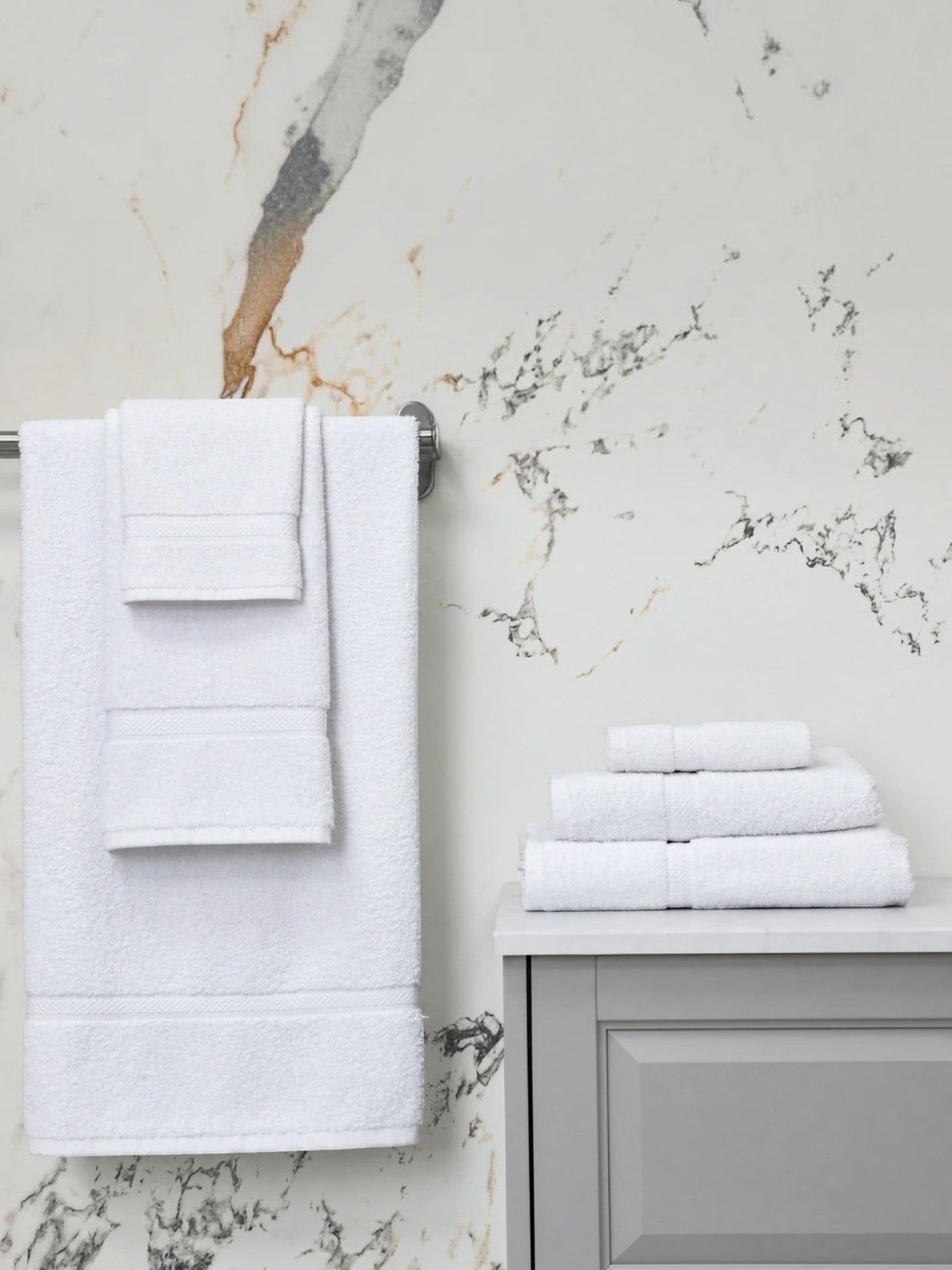 Valiant Products Brentwood white ring-spun cotton hand towels with dobby border hanging and stacked in a bathroom.