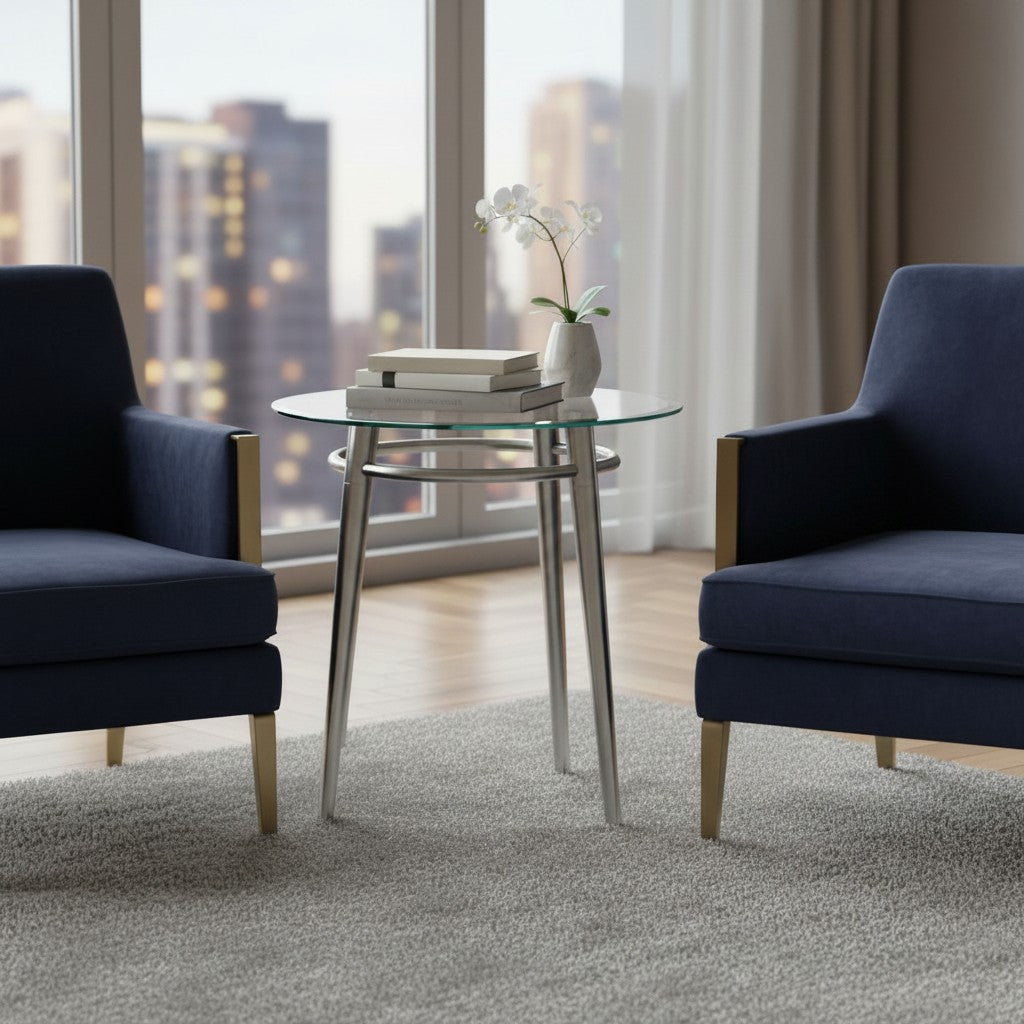 Valiant Products Brooklyn round glass end table with brushed nickel metal legs placed between two navy armchairs.