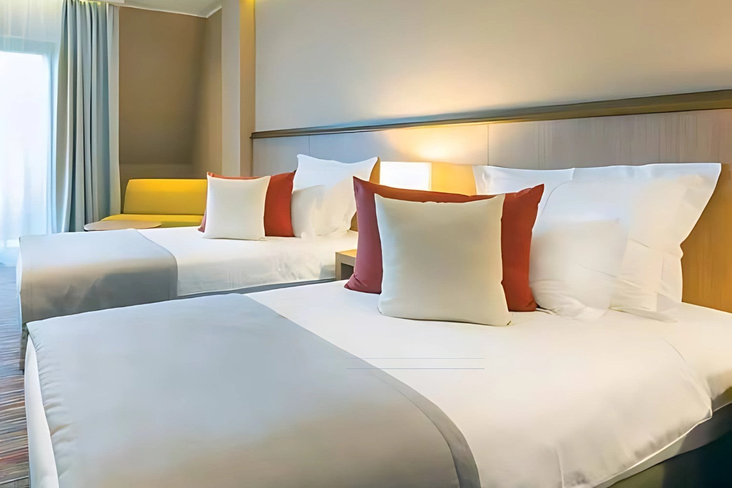 Valiant Products commercial-grade white fitted sheets on hotel beds with decorative pillows in a modern guest room