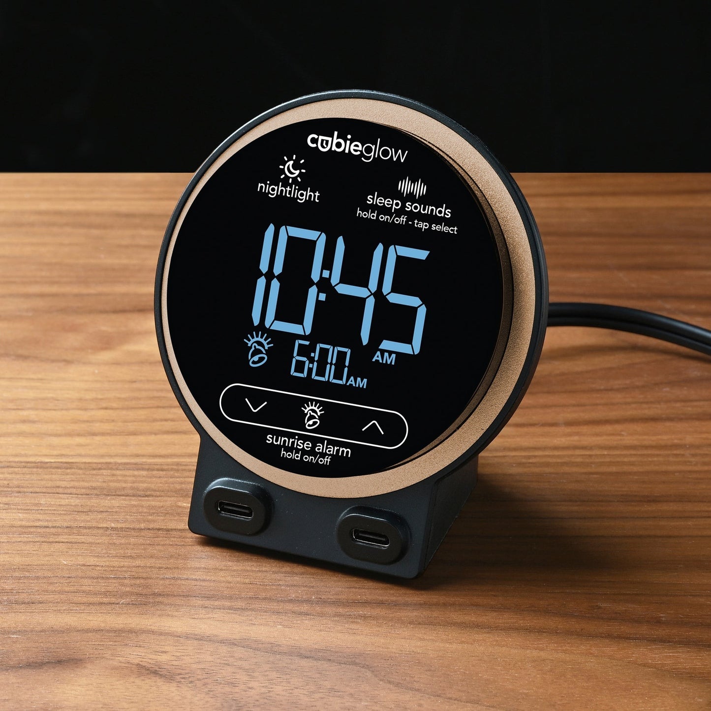 Valiant Products CubieGlow black digital alarm clock with dual USB-C ports and sunrise alarm feature on a wood table.