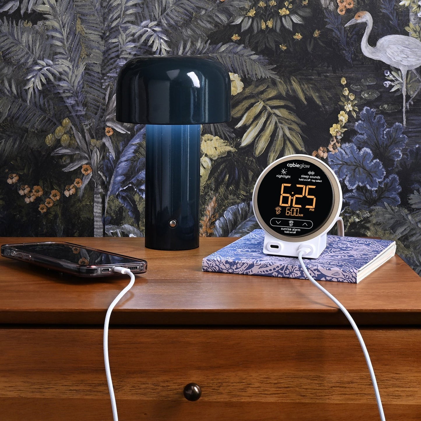 Valiant Products CubieGlow white charging alarm clock with USB-C ports on a wooden nightstand next to a lamp.