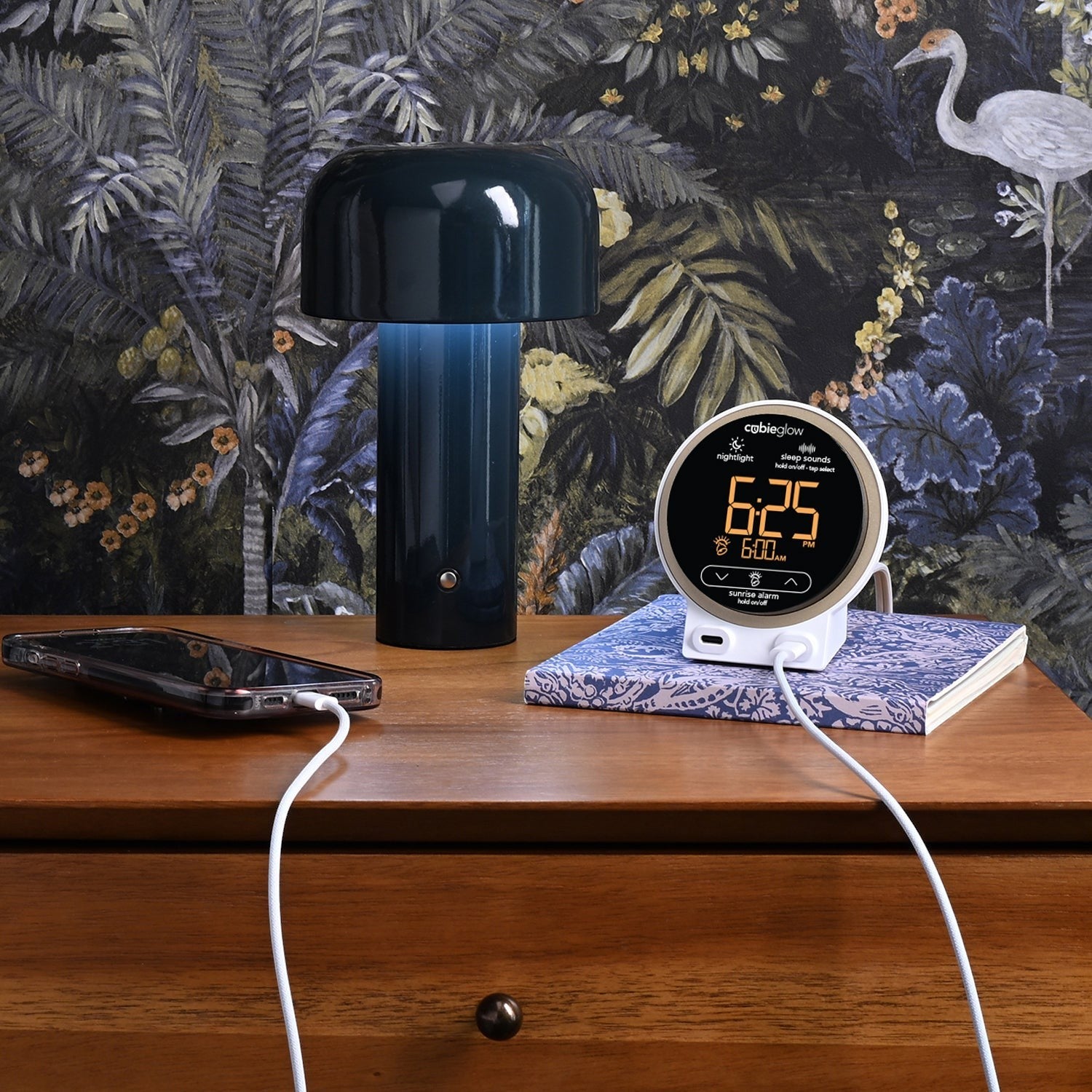 Valiant Products CubieGlow white charging alarm clock with USB-C ports on a wooden nightstand next to a lamp.