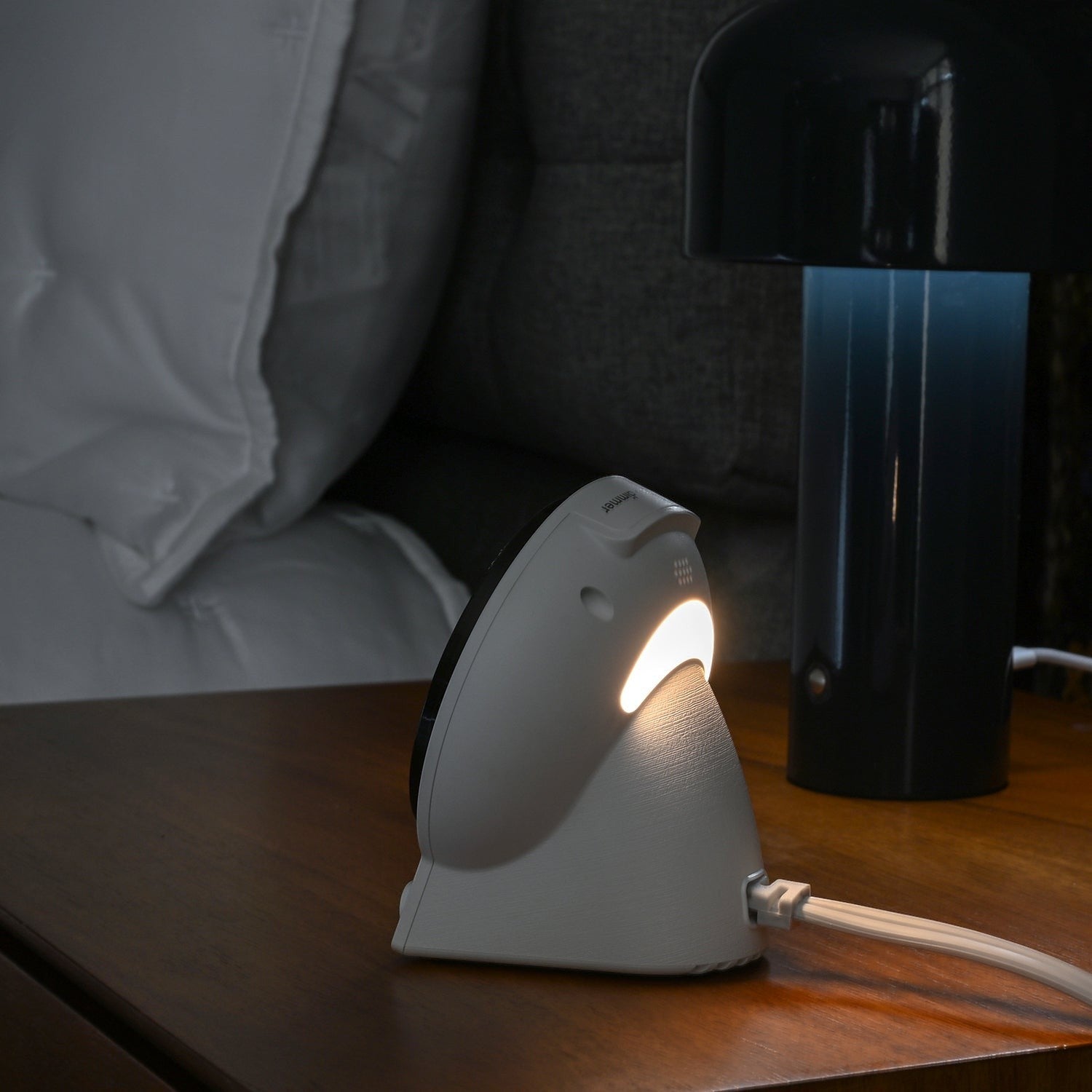 Valiant Products CubieGlow white charging alarm clock with glowing night light on a wooden hotel nightstand
