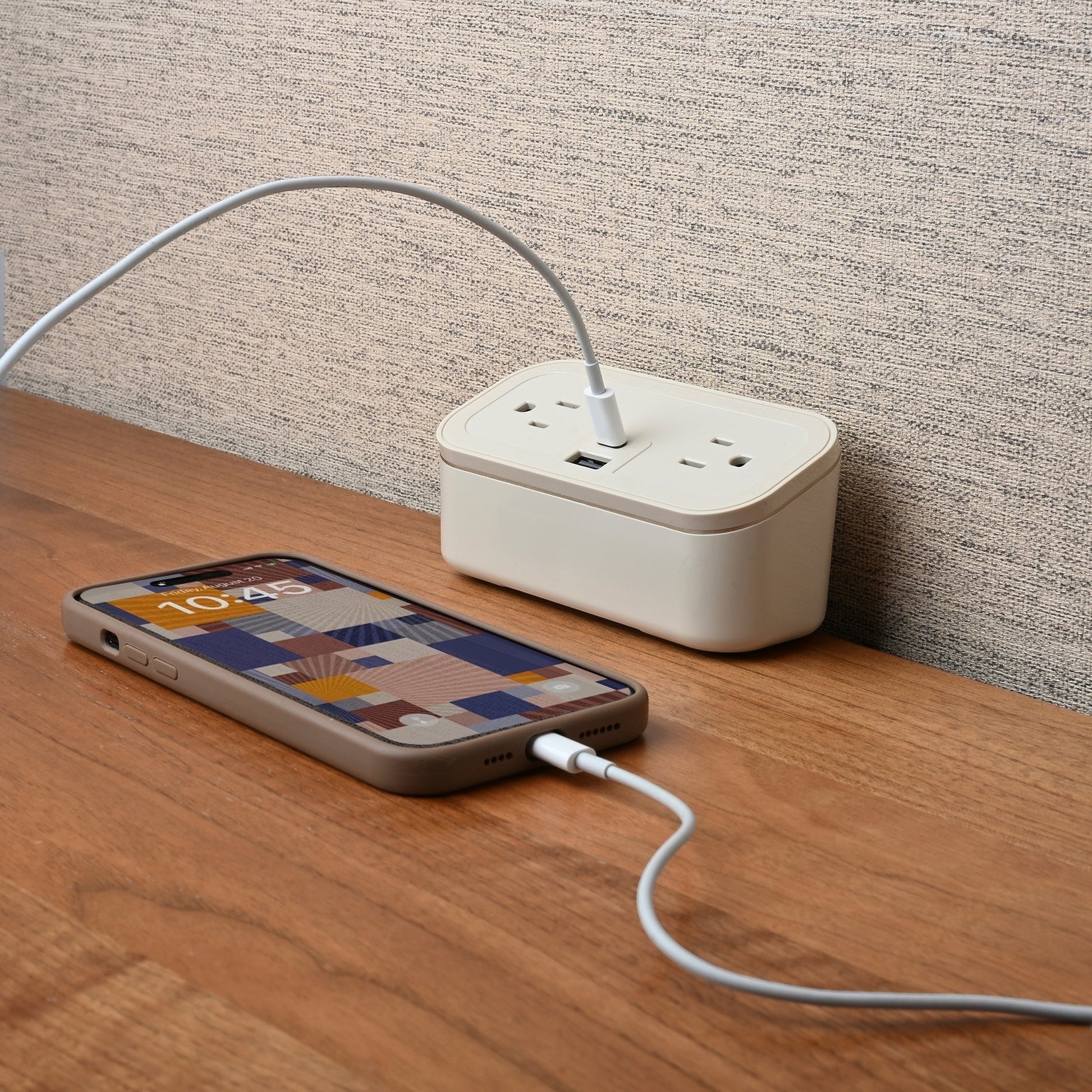 Valiant Products CubieMini white charging block with two outlets, USB-A, and USB-C ports charging a smartphone.