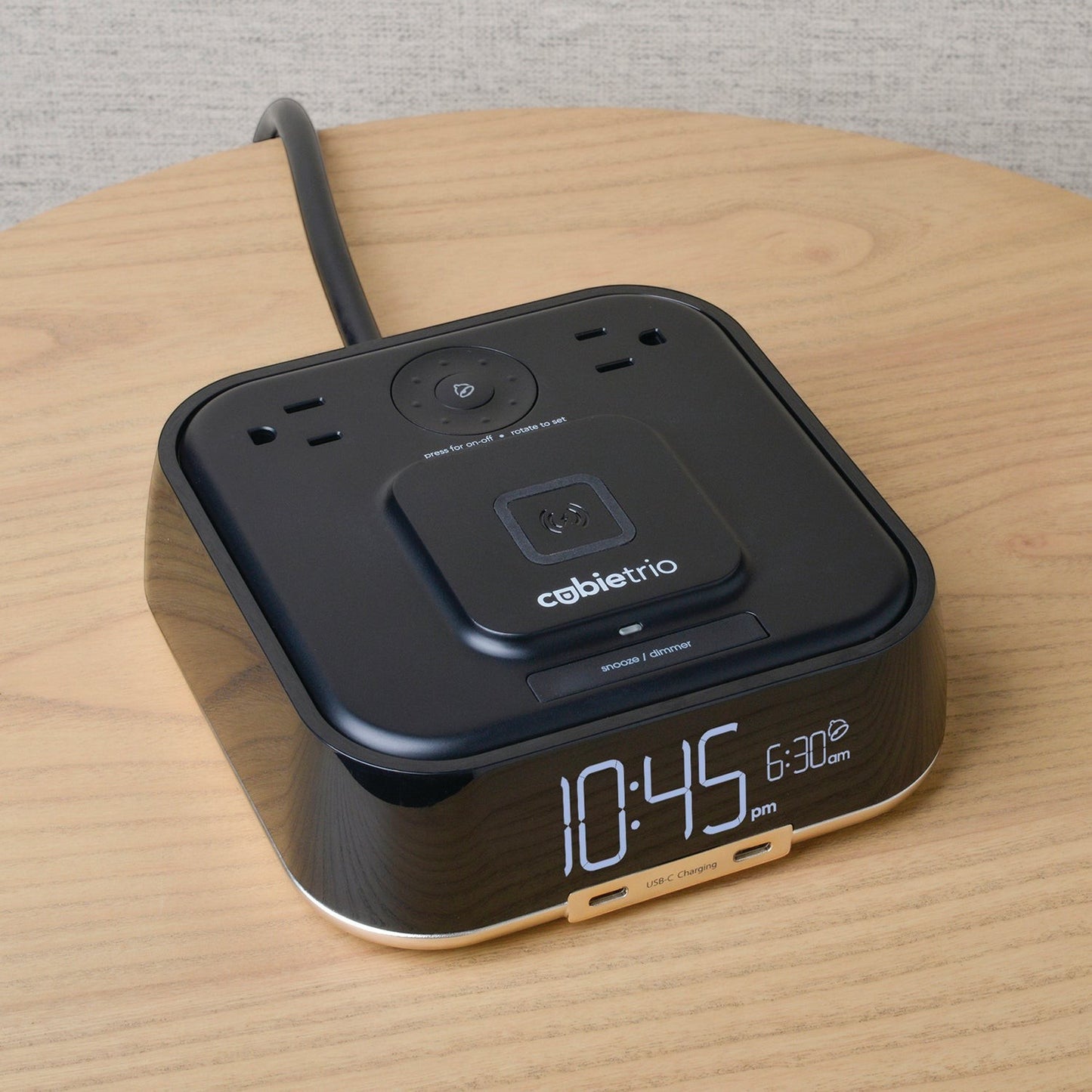 Valiant Products CubieTrio black alarm clock with wireless charging pad, USB-C ports, and power outlets on a wooden table