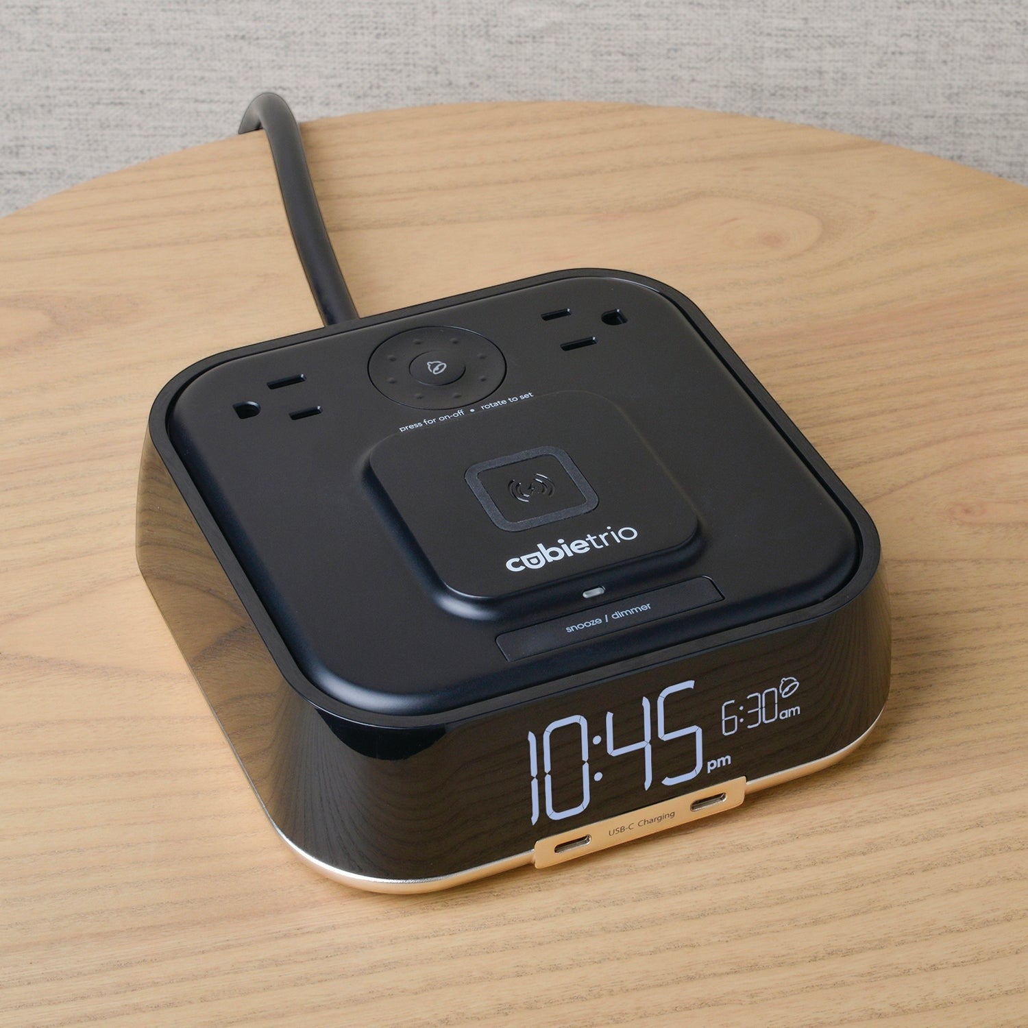 Valiant Products CubieTrio black alarm clock with wireless charging pad, USB-C ports, and power outlets on a wooden table
