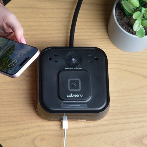 Valiant Products CubieTrio black alarm clock with wireless charging pad, USB-C ports, and power outlets on a desk.