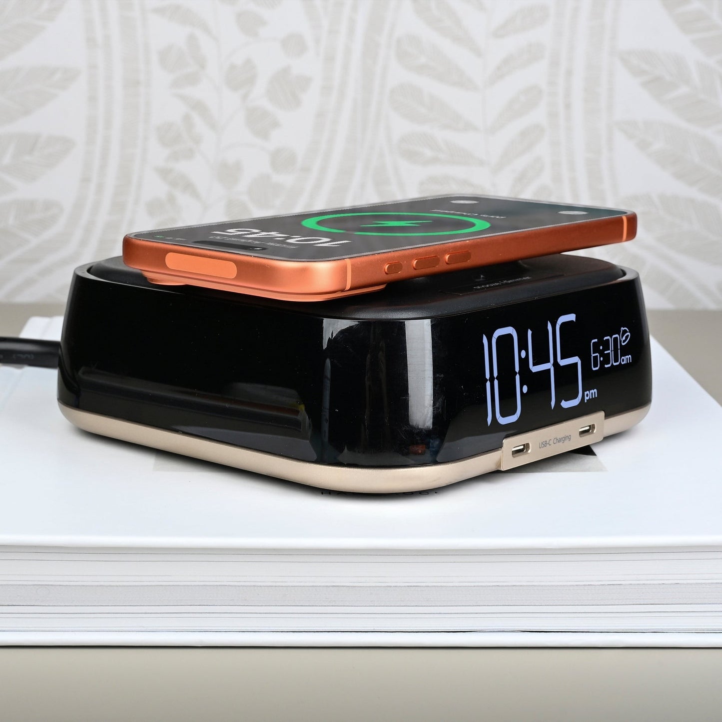 Valiant Products CubieTrio black and champagne alarm clock with a smartphone charging wirelessly on top