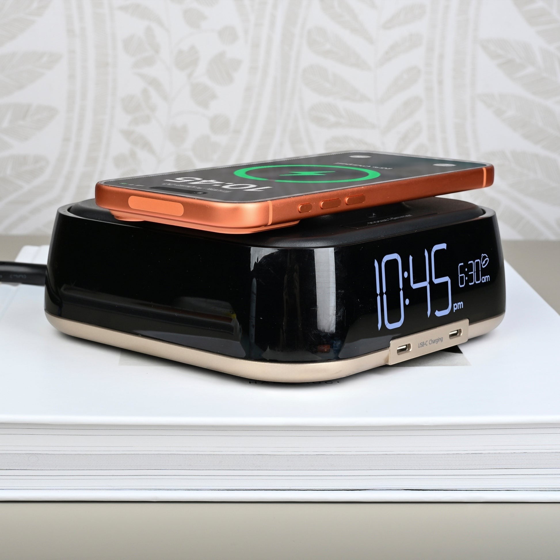 Valiant Products CubieTrio black and champagne alarm clock with a smartphone charging wirelessly on top