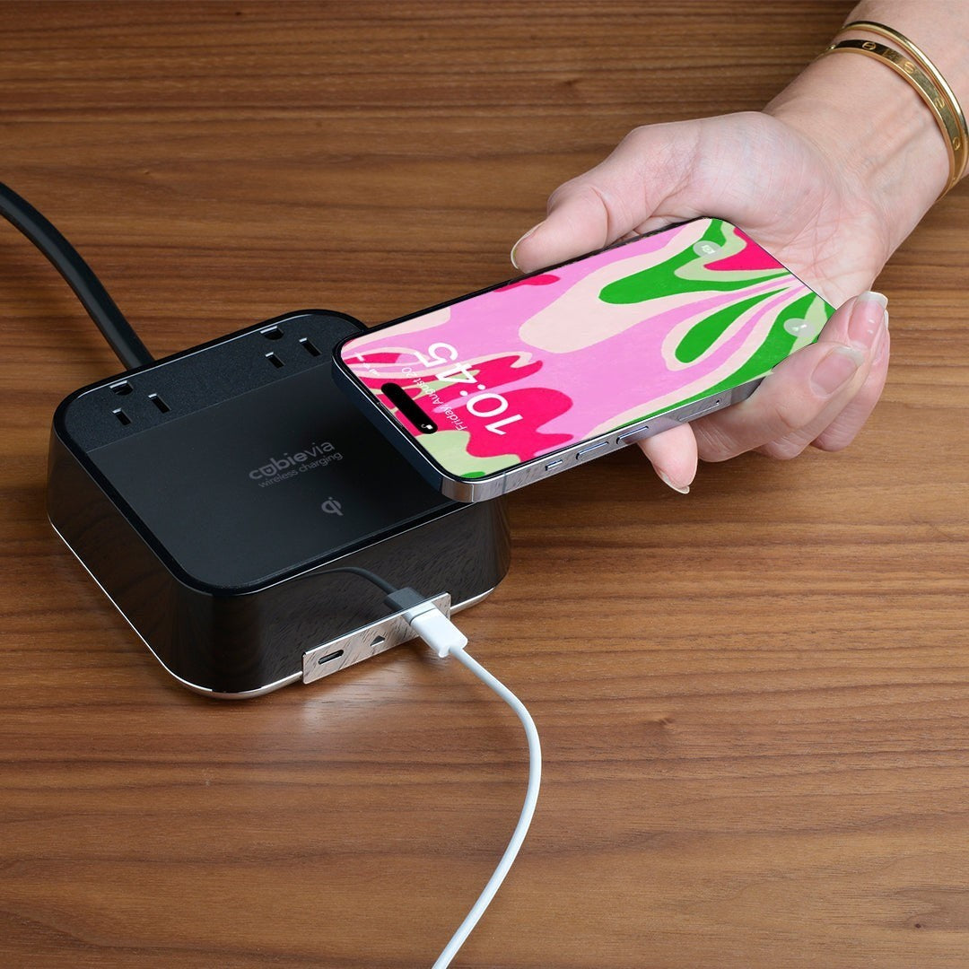 Valiant Products CubieVia black charging block with wireless Qi pad, two AC outlets, and USB-C ports on a wood desk.