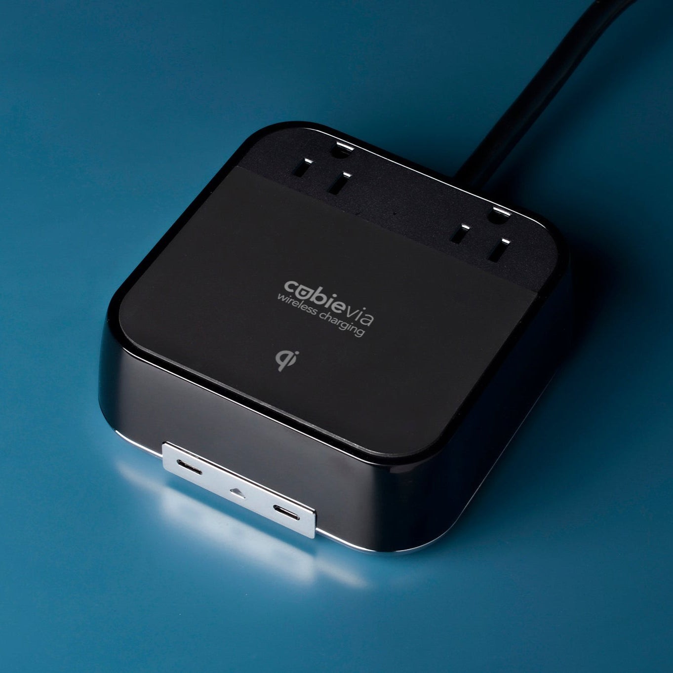 Valiant Products CubieVia black charging block with Qi wireless charging, AC outlets, and USB-C ports on blue surface