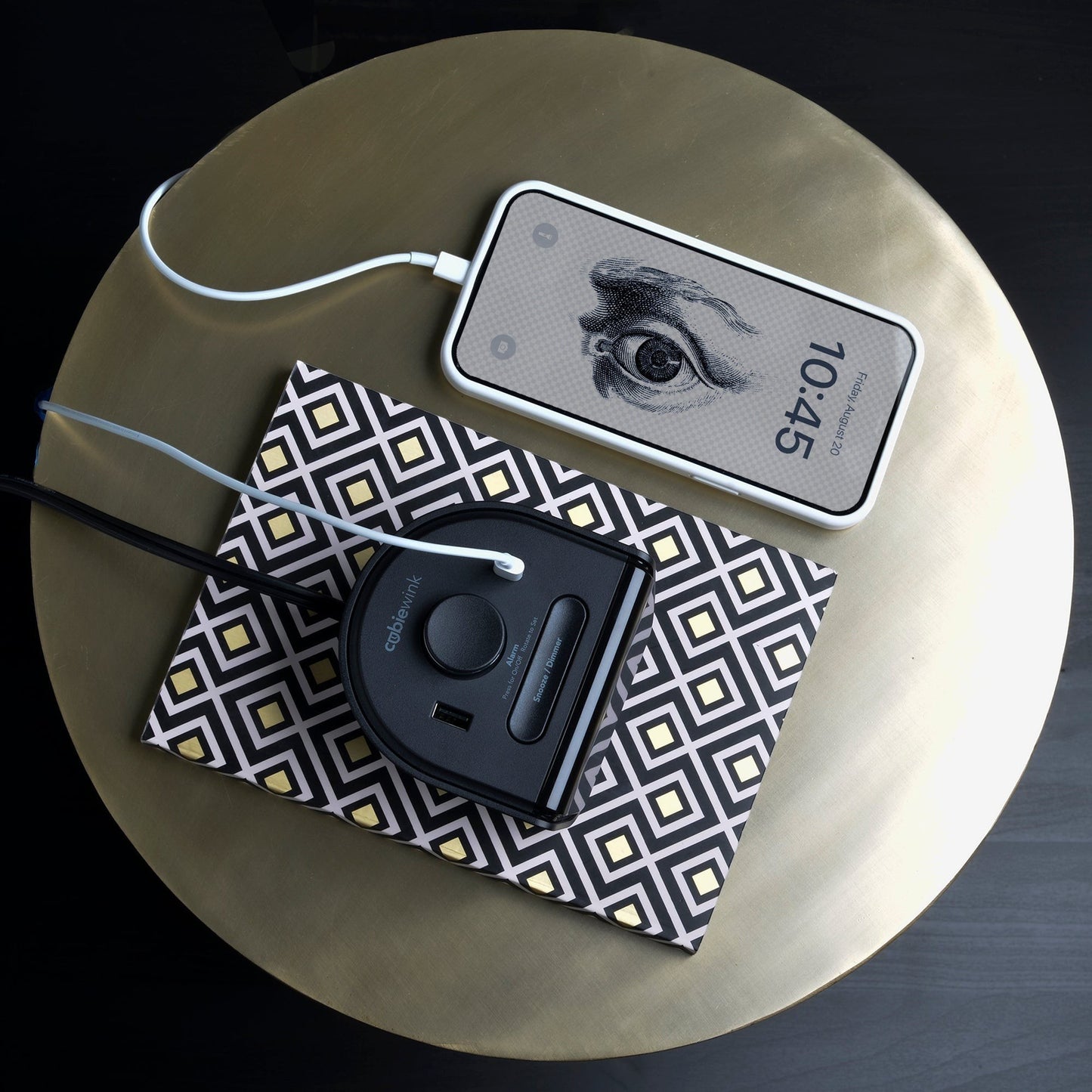 Valiant Products CubieWink black alarm clock with USB-C and USB-A charging ports on a patterned notebook and table