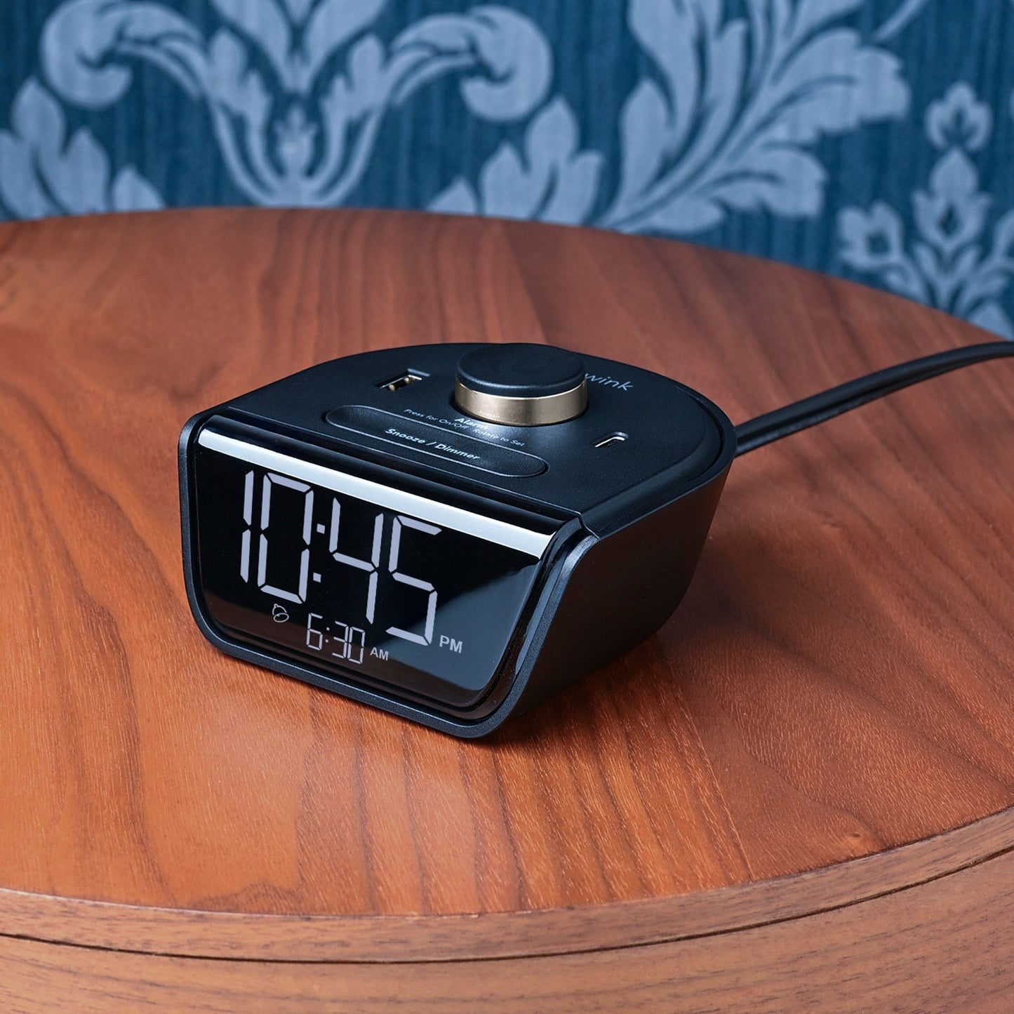 Valiant Products CubieWink black compact alarm clock with USB-A and USB-C ports on a wooden nightstand