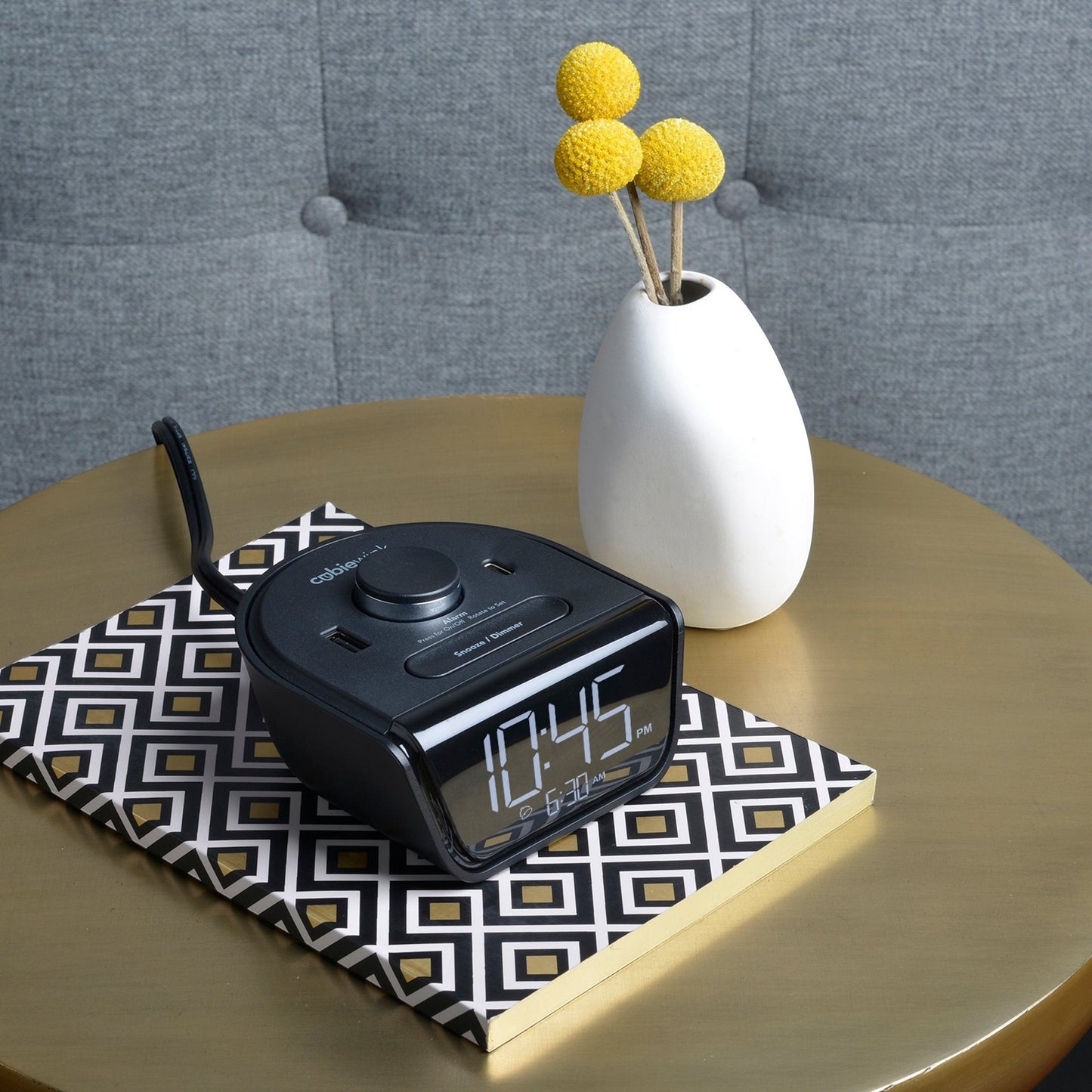 Valiant Products CubieWink black alarm clock with USB-A and USB-C ports on a patterned notebook on a gold table