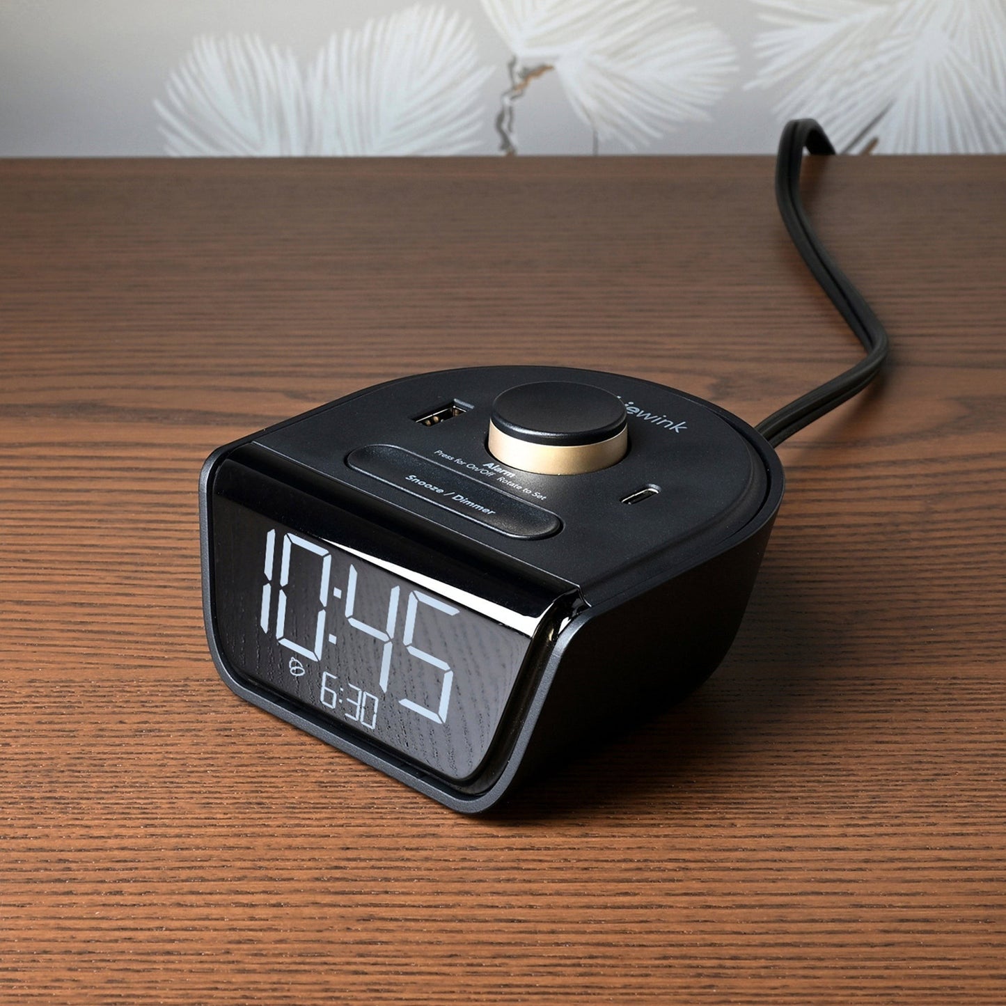 Valiant Products CubieWink black compact alarm clock with USB-A and USB-C charging ports on a wooden nightstand.