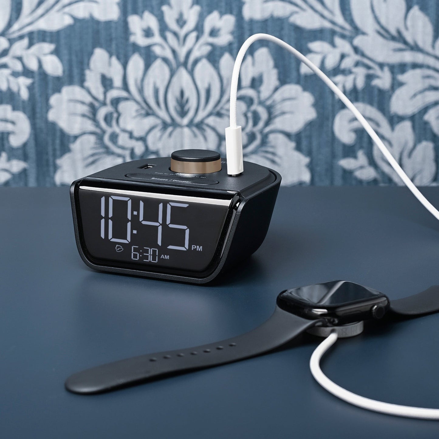 Valiant Products CubieWink black alarm clock with USB-C and USB-A charging ports on a dark desk with a smartwatch.