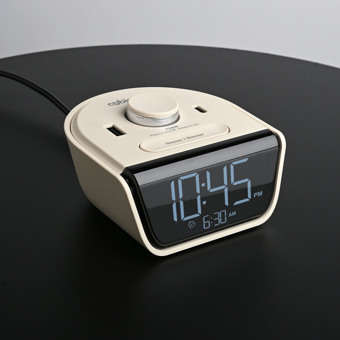 Valiant Products CubieWink latte-colored compact alarm clock with USB-A and USB-C charging ports on a black surface.