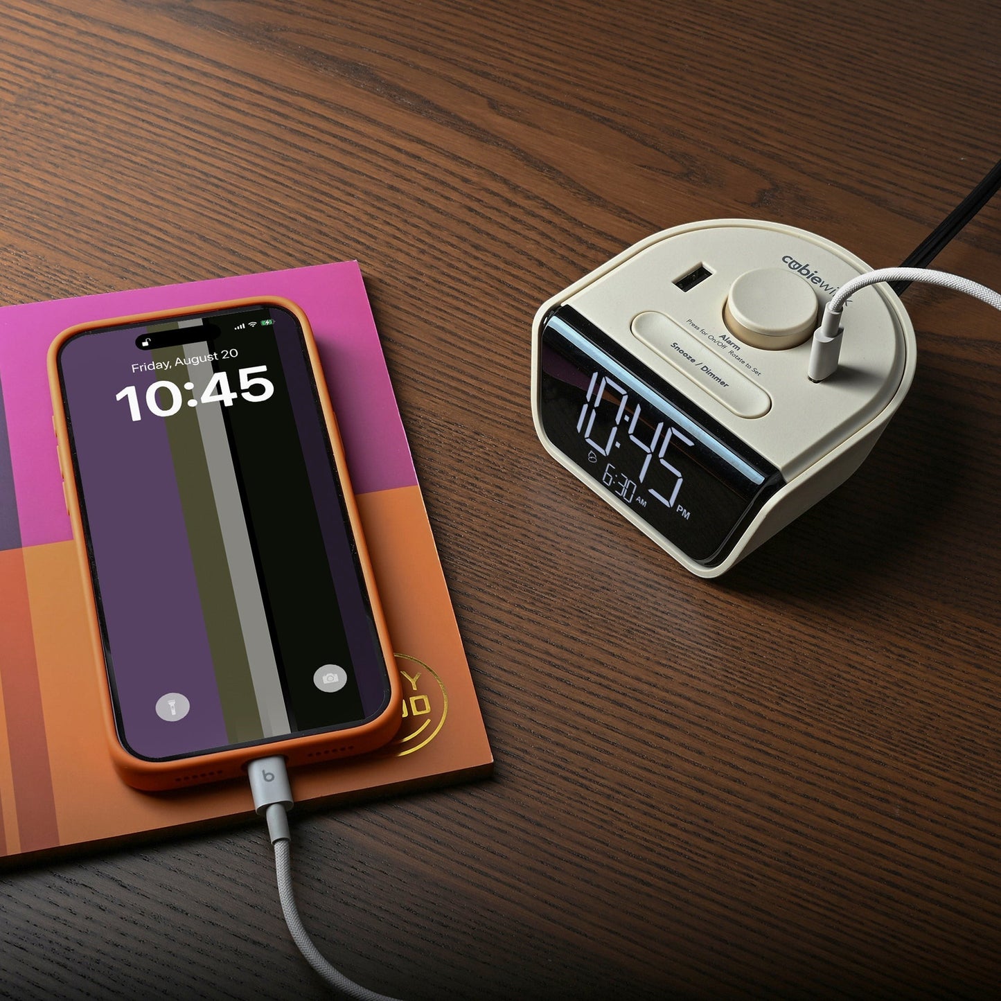 Valiant Products CubieWink latte charging alarm clock with USB-A and USB-C ports charging a smartphone on a desk.