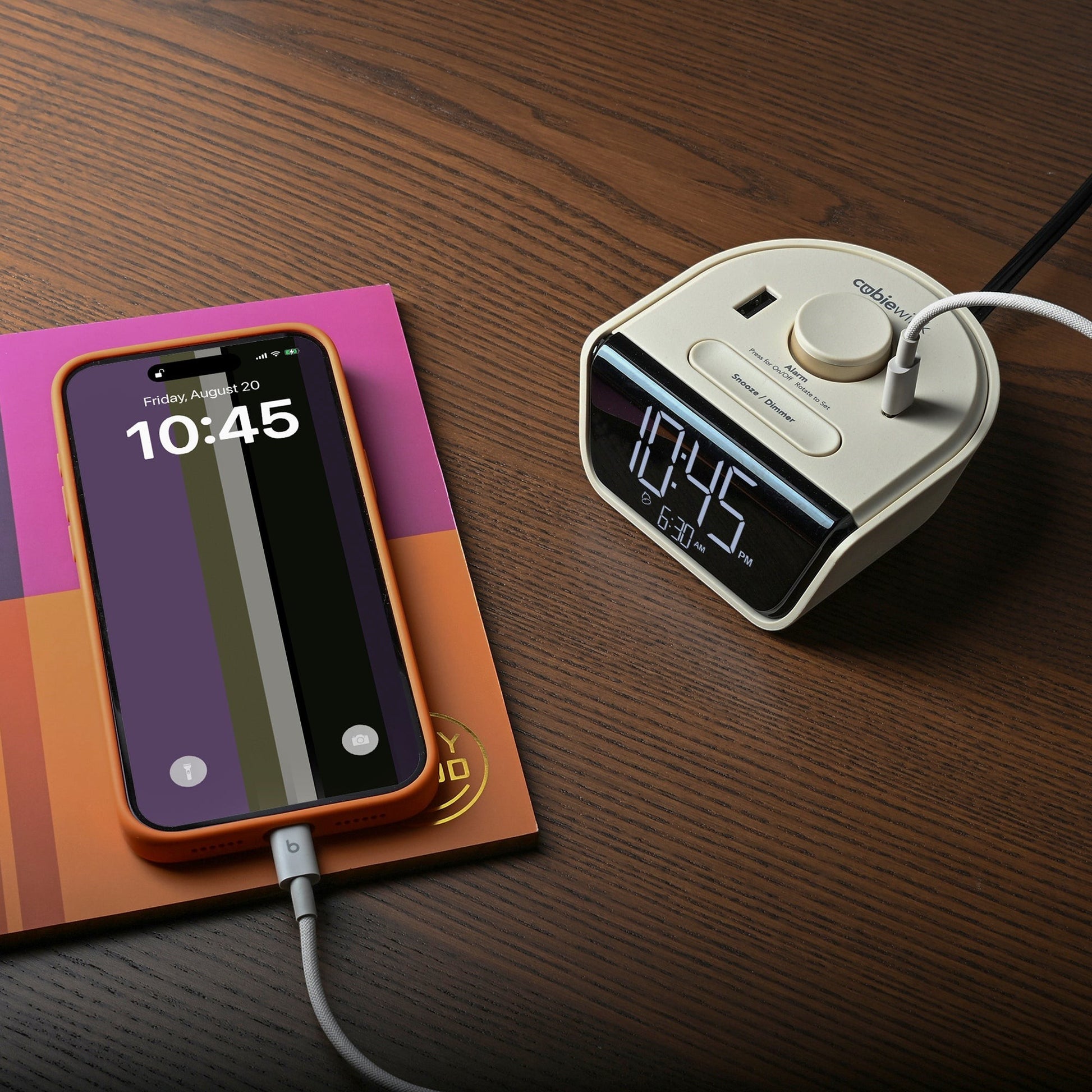 Valiant Products CubieWink latte charging alarm clock with USB-A and USB-C ports charging a smartphone on a desk.