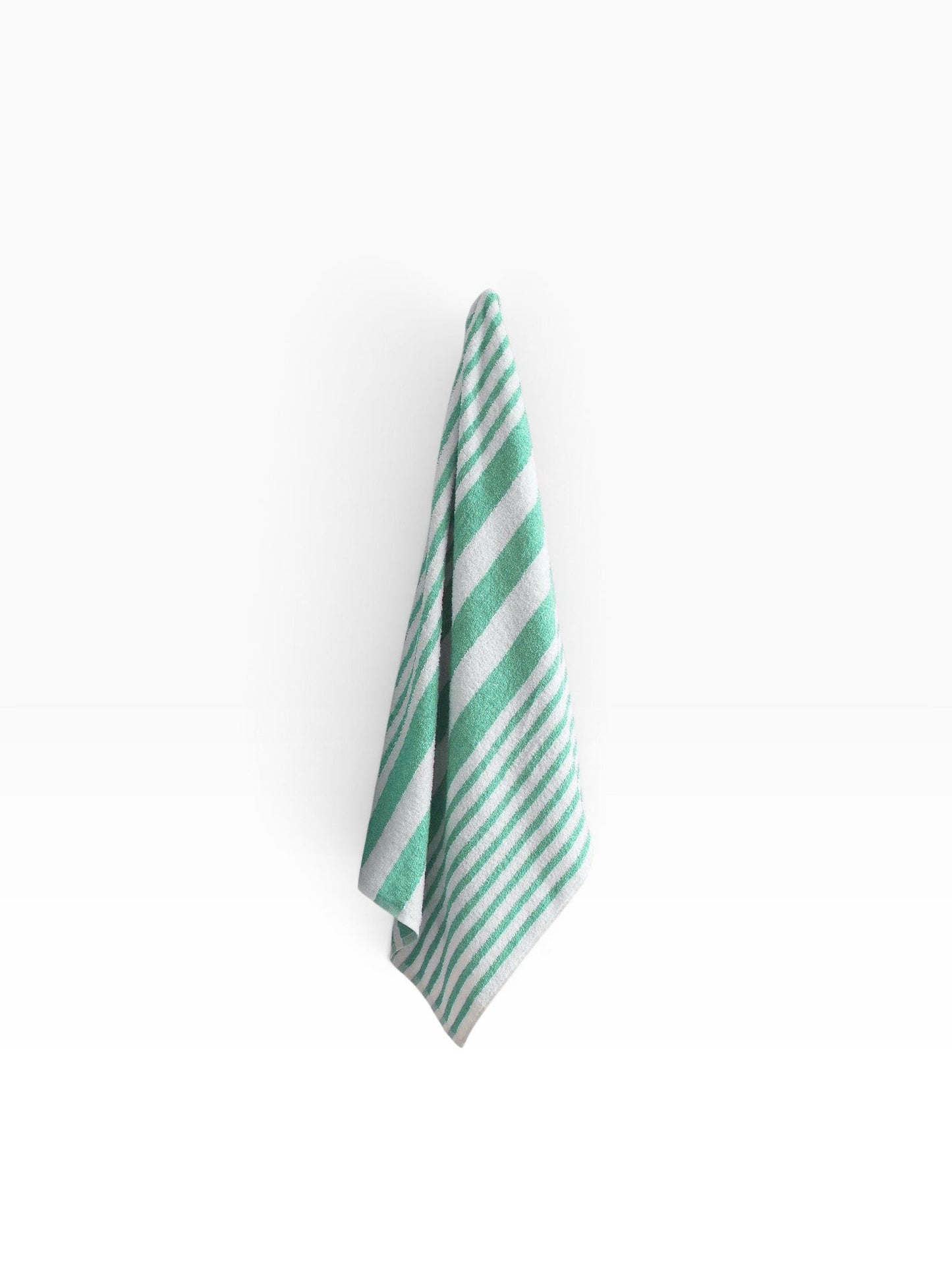 Valiant Products Tropical Stripe borderless pool towel in white and jade green cotton hanging against a white wall.