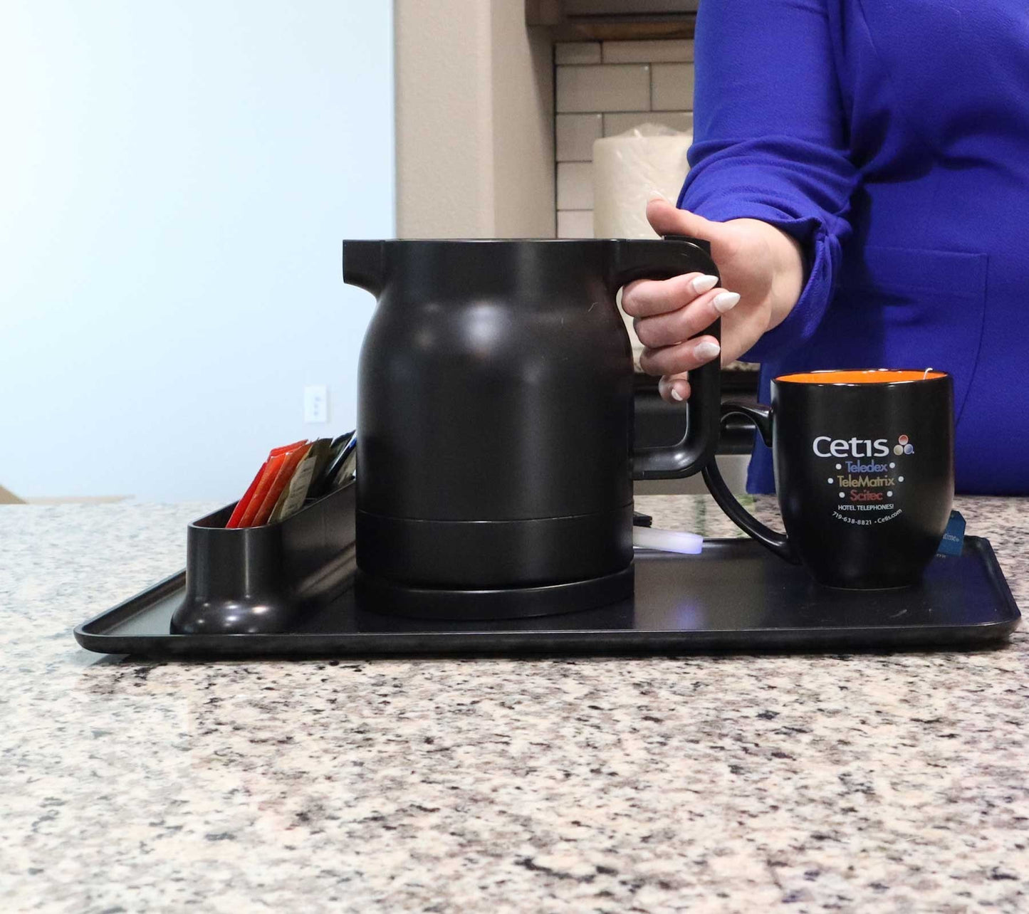 Valiant Products K-100 black electric kettle on a hotel hospitality tray with a matching mug and tea packets.