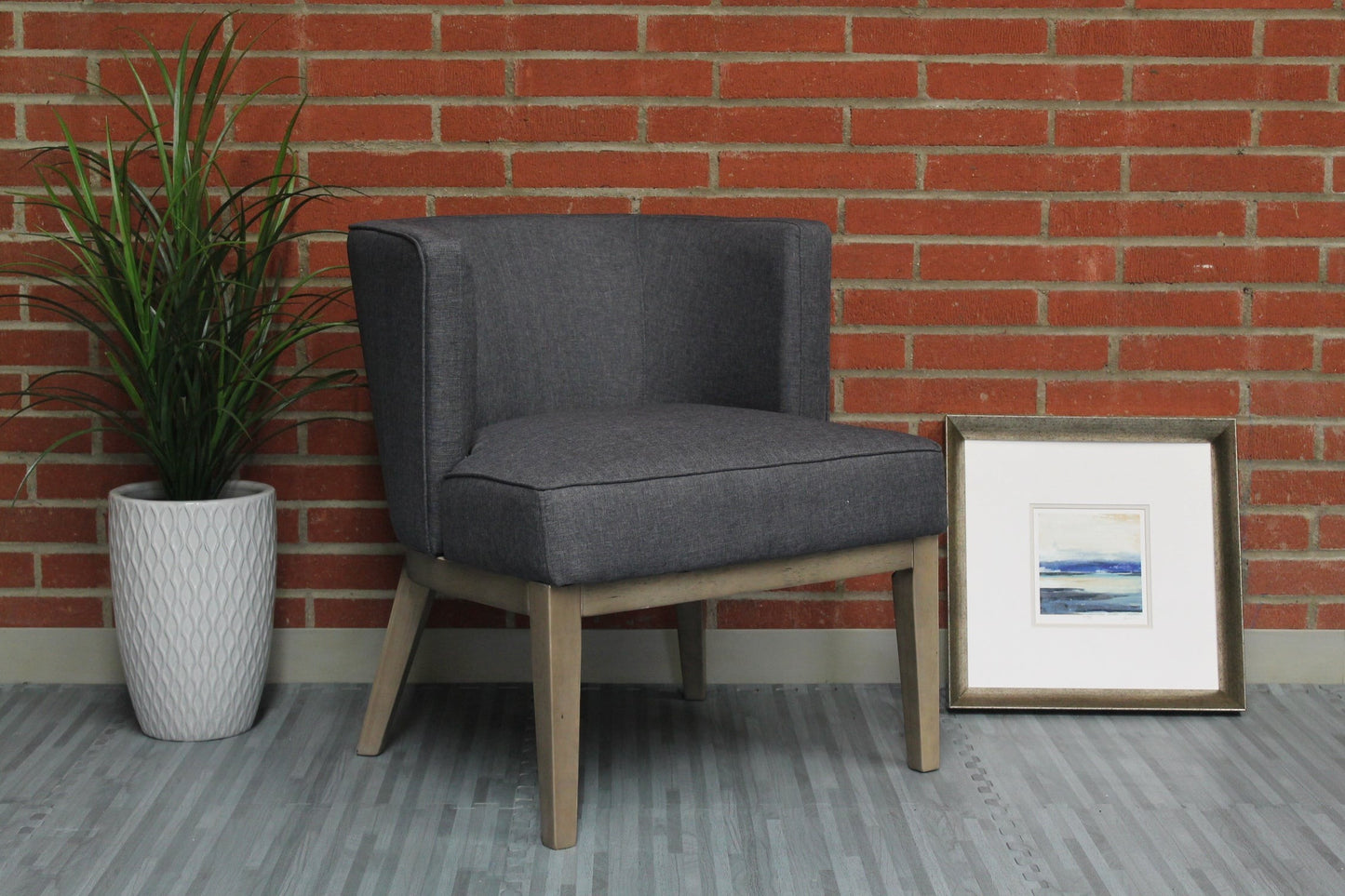 Valiant Products Langford accent chair in grey linen with wooden legs against a brick wall