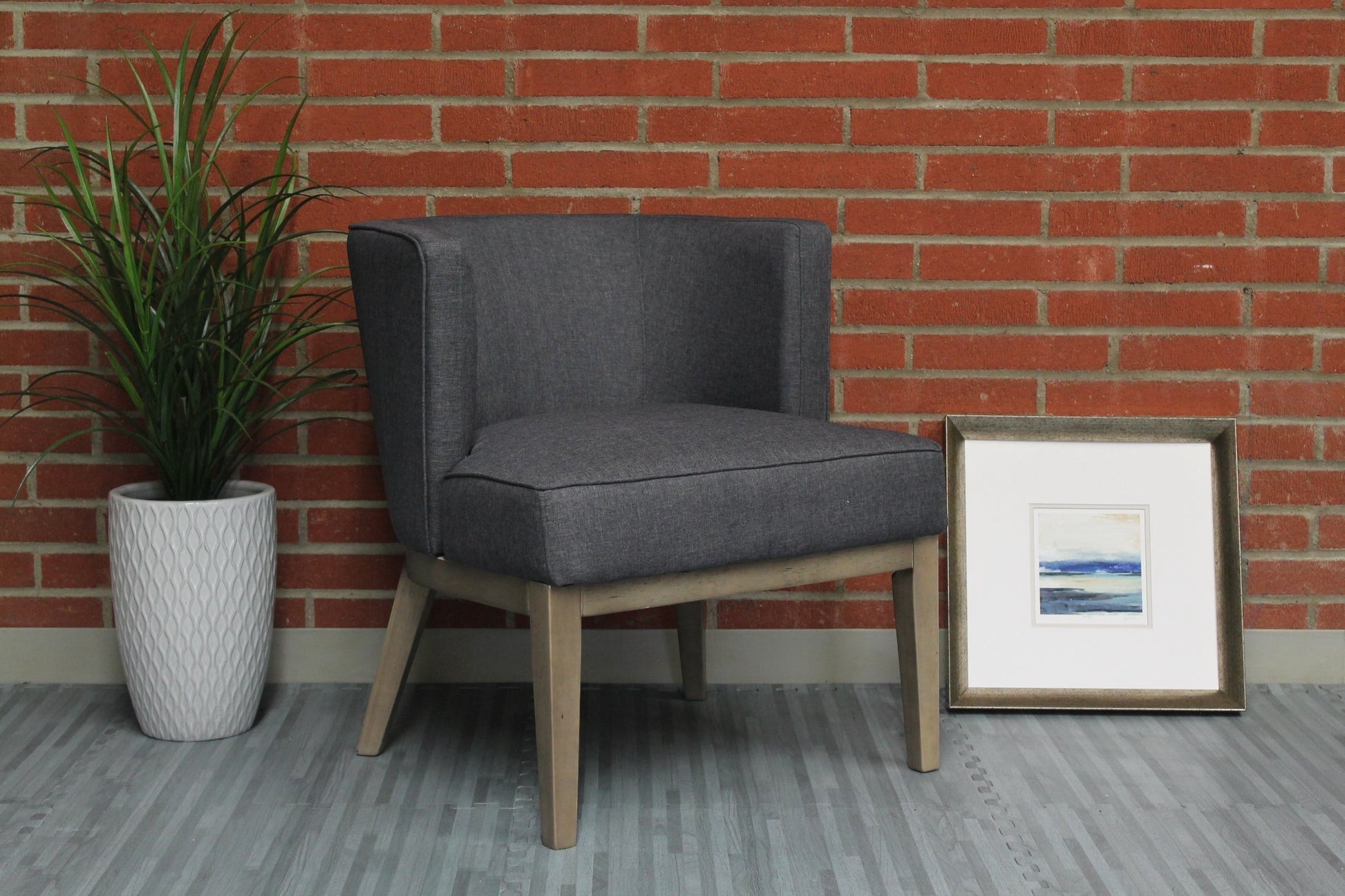 Valiant Products Langford accent chair in grey linen with wooden legs against a brick wall