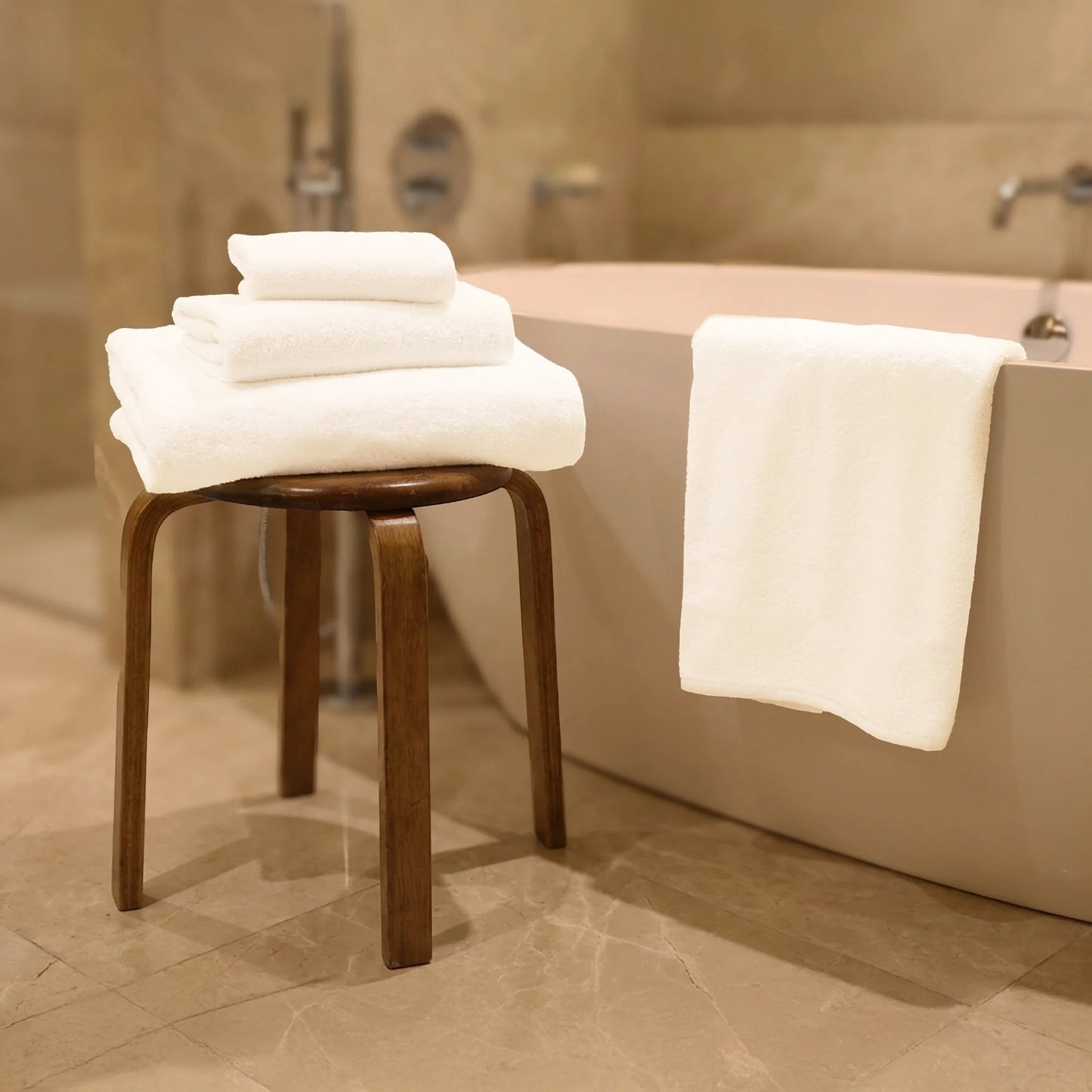 Valiant Products Luxe white borderless cotton bath towels stacked on a wooden stool in a modern bathroom setting