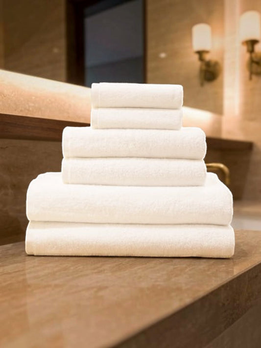 Valiant Products Luxe white borderless cotton bath towels stacked neatly on a marble bathroom vanity