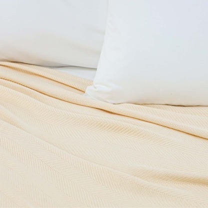 Valiant Products Atelier Luxe natural herringbone weave blanket made from cotton and TENCEL Modal fibers on a bed