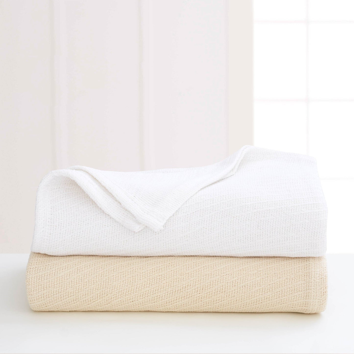 Valiant Products Sovereign cotton blankets in white and natural stacked on a table with a tight diagonal weave.