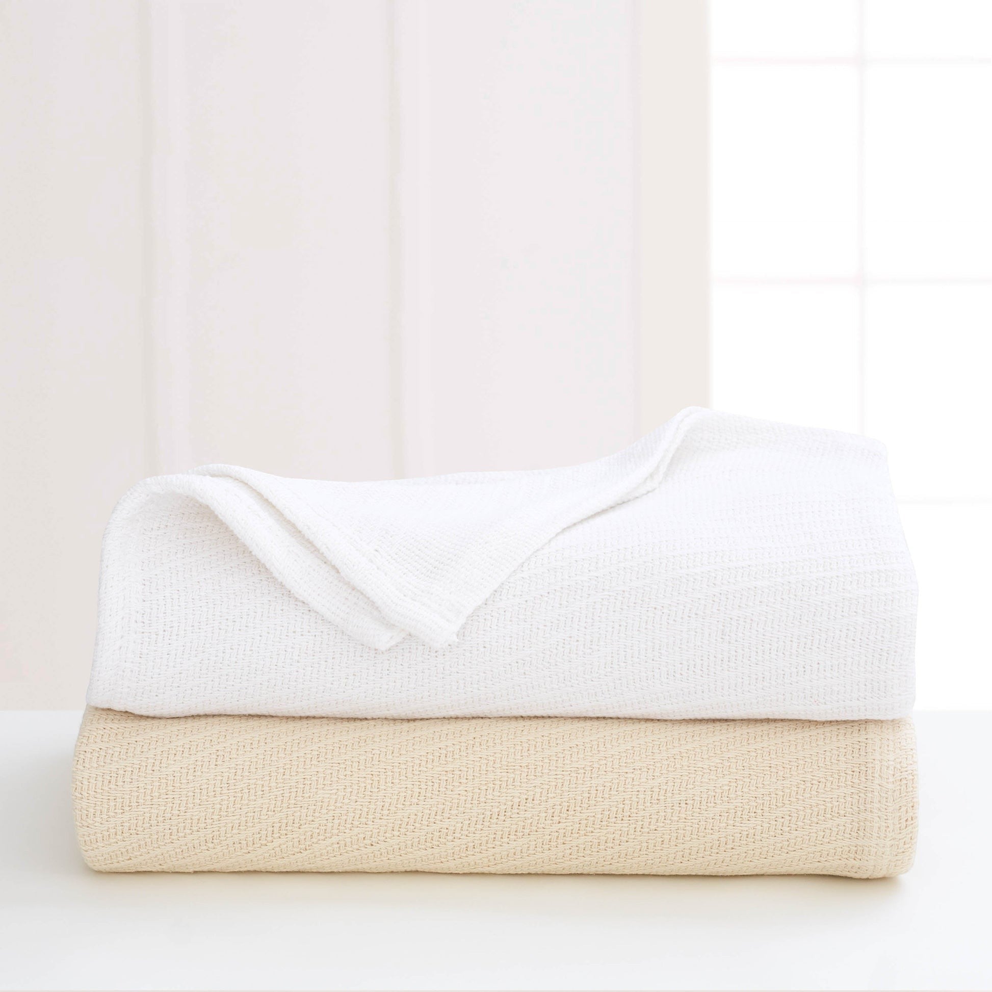 Valiant Products Sovereign cotton blankets in white and natural stacked on a table with a tight diagonal weave.