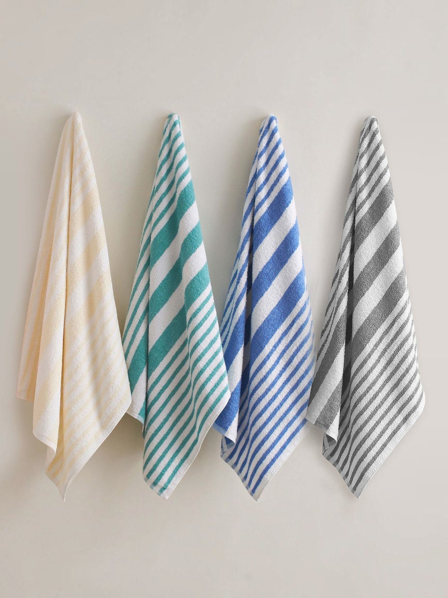 Valiant Products cotton pool towels in pastel yellow, jade, blue, and grey stripes hanging against a neutral wall.