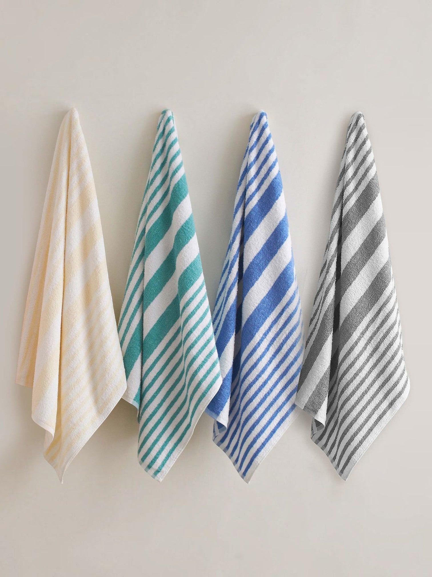 Valiant Products cotton pool towels in pastel yellow, jade, blue, and grey stripes hanging against a neutral wall.