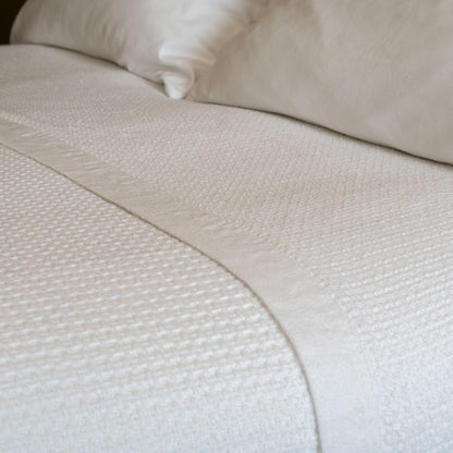 Valiant Products white cotton blanket featuring a textured basketweave pattern and a tailored hem on a made bed.