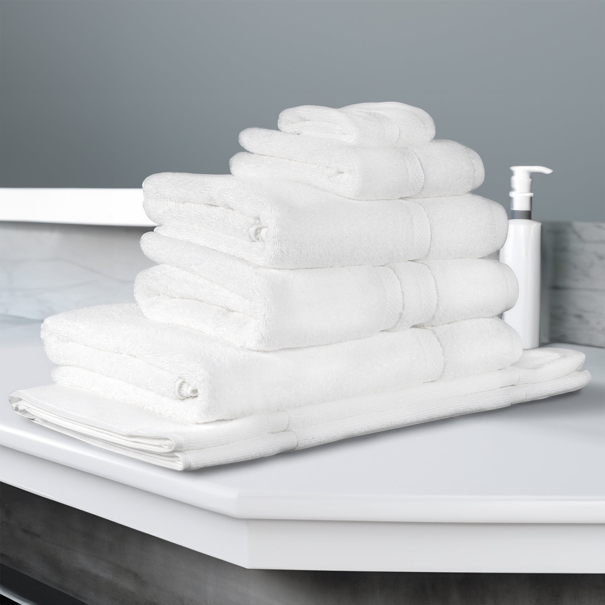 Valiant Products white Simplicity dobby border cotton bath towels stacked on a bathroom vanity