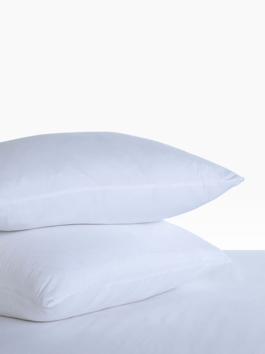 Valiant Products white microfiber pillow protectors stacked on a bed for hospitality use