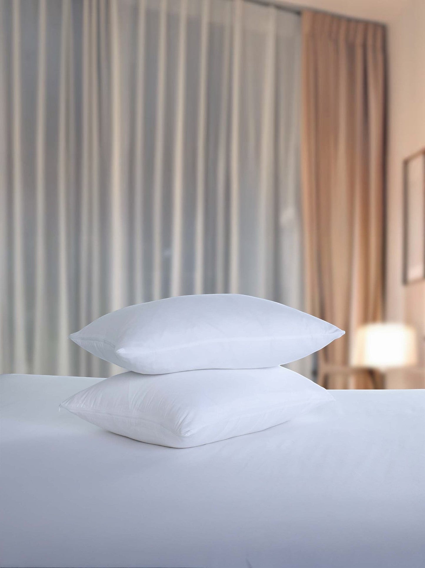 Valiant Products white brushed microfiber pillow protectors stacked on a bed in a hotel room setting