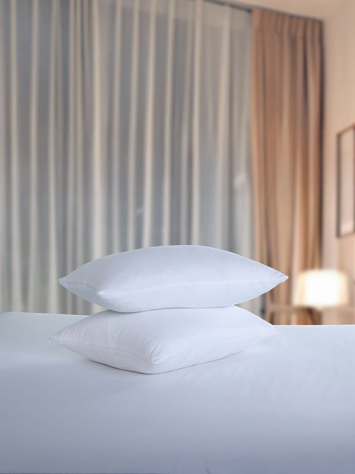 Valiant Products white brushed microfiber pillow protectors stacked on a bed in a hotel room setting