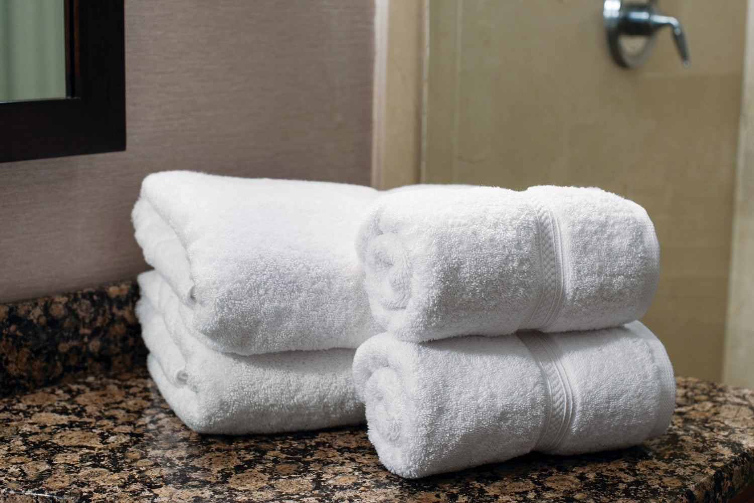 Valiant Products white plush cotton bath mats with textured dobby border design stacked on a granite bathroom vanity.