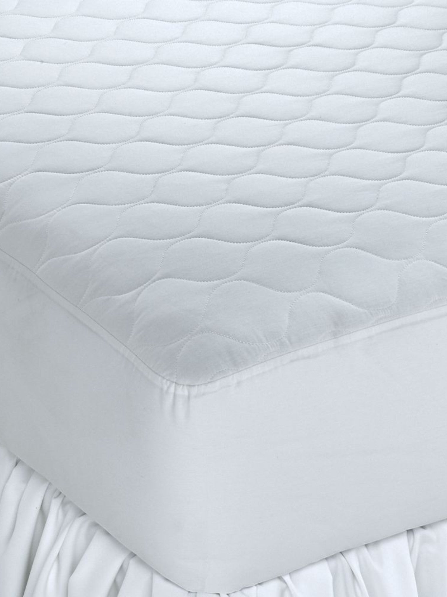 Valiant Products white Ultra Touch quilted mattress pad with ogee pattern and fitted elastic skirt on a bed