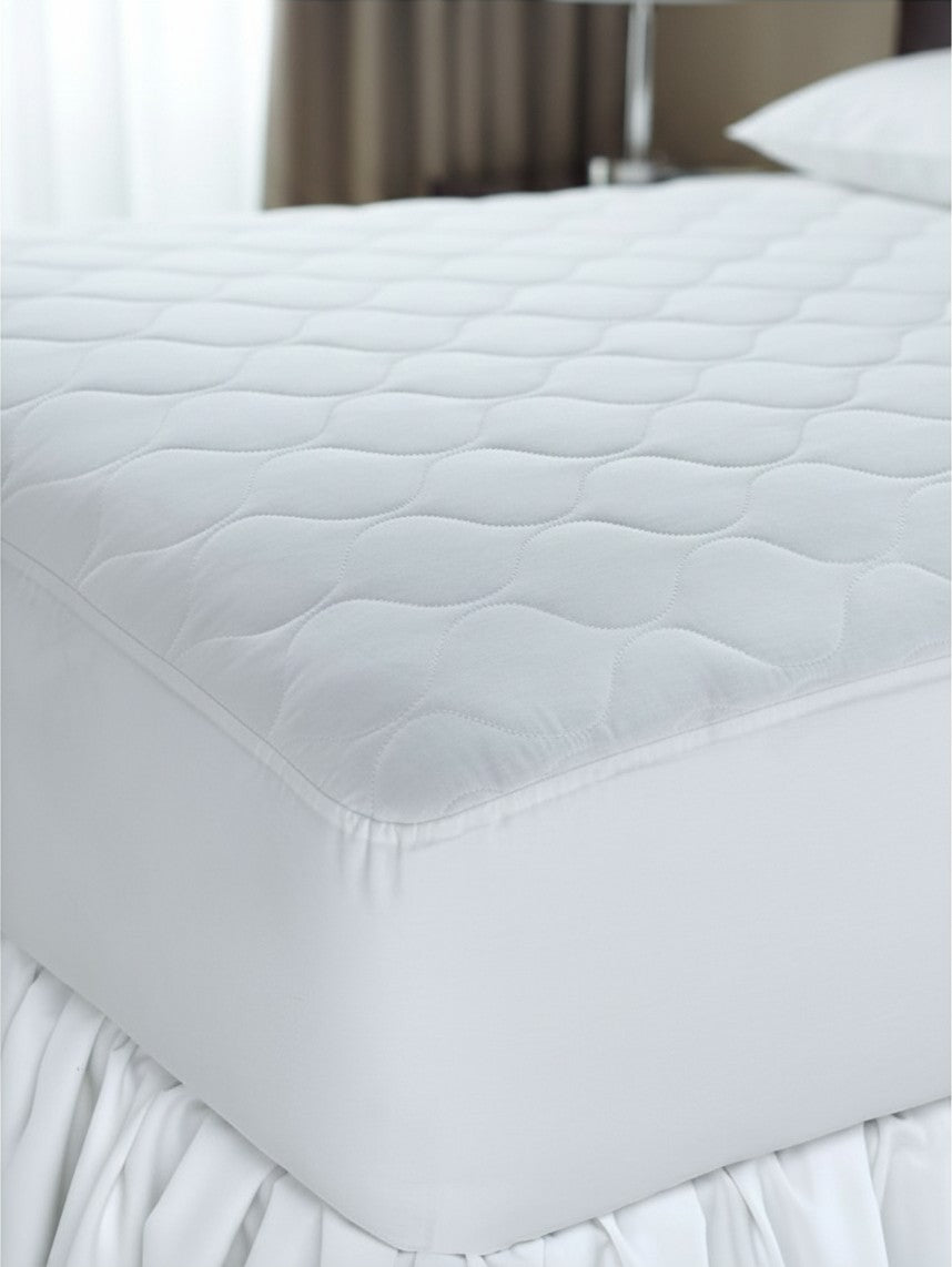 Valiant Products Ultra Touch white quilted mattress pad with ogee pattern and fitted elastic skirt on a bed