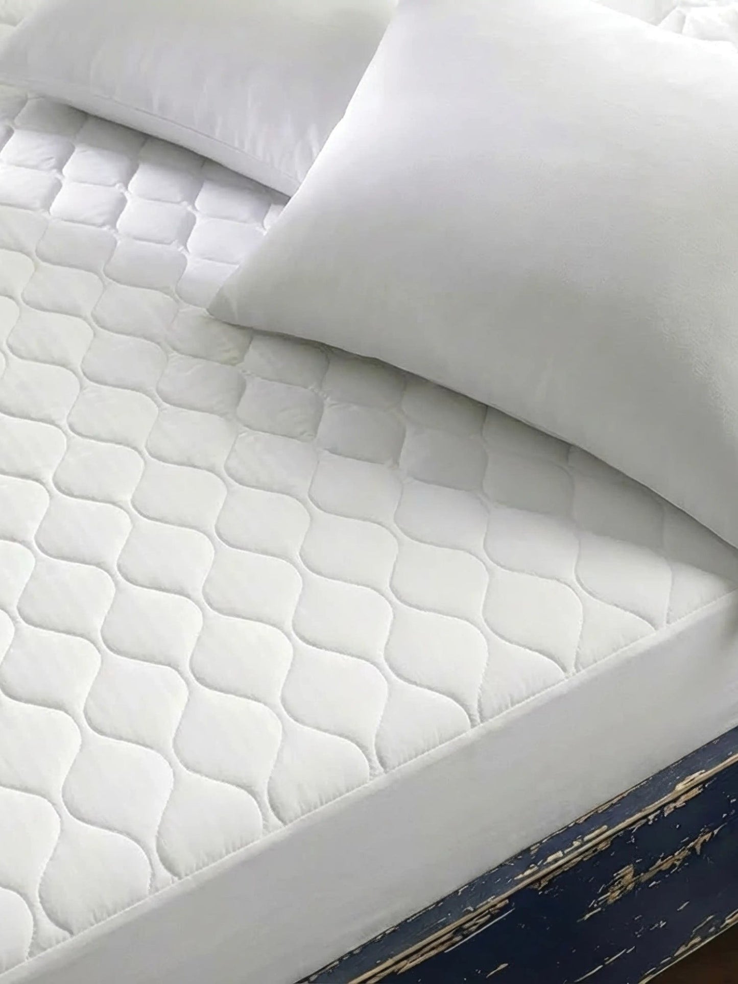 Valiant Products white quilted mattress pad with ogee pattern on a bed with pillows